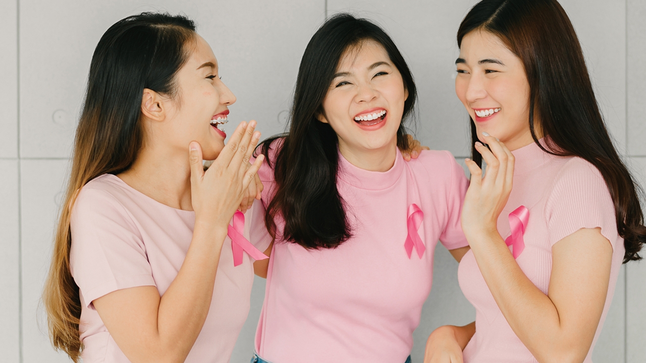 Three girls wearing pink shirts are chatting ; image used for the High-Risk Breast Surveillance Programme sponsored by HSBC Life.